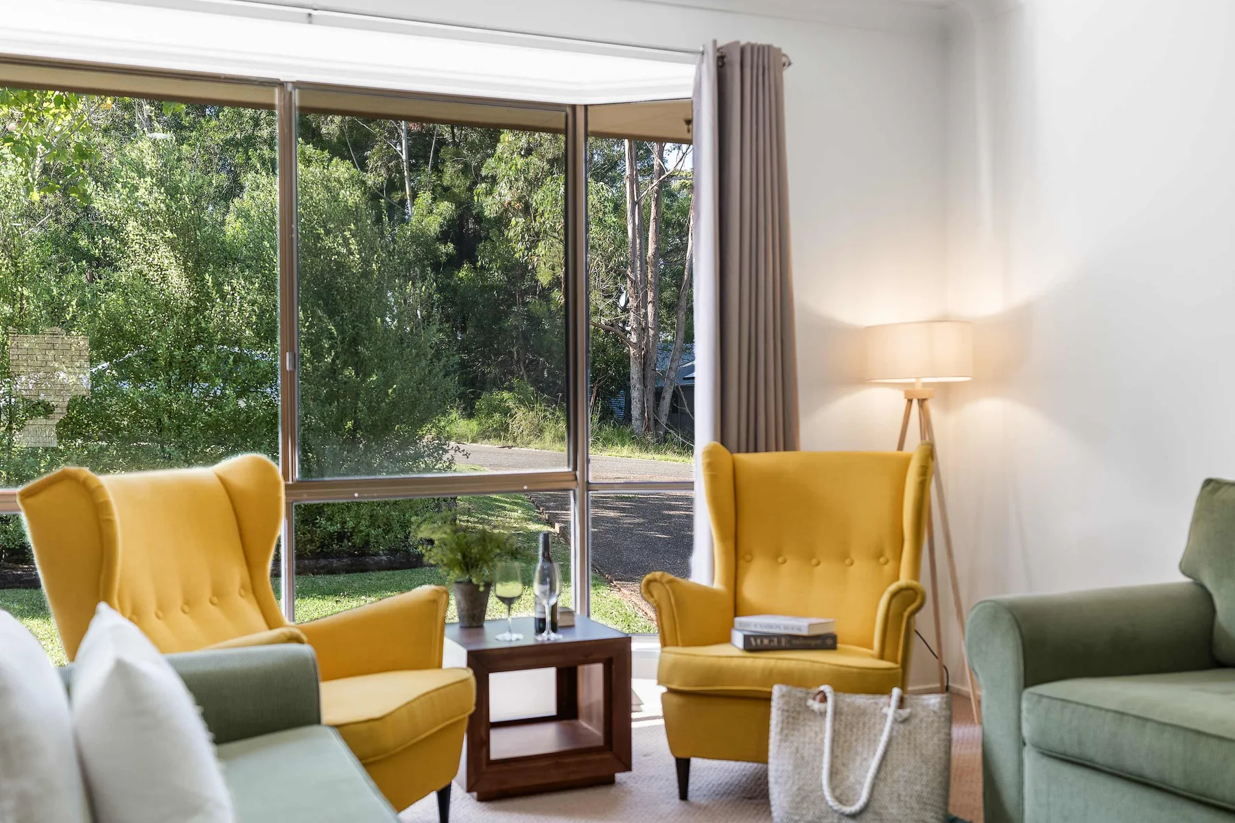 A bright living room with yellow seating beside large windows overlooking greenery.
