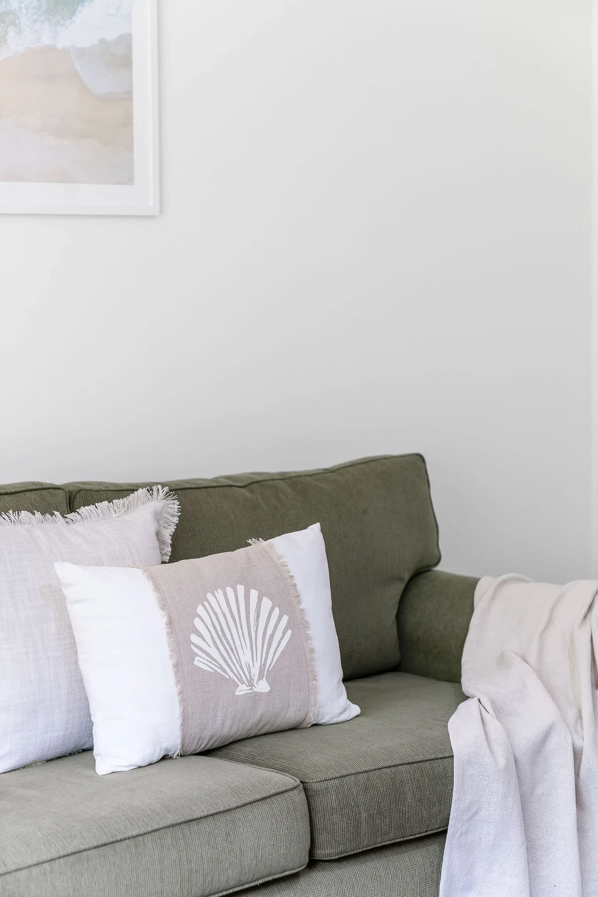 A green sofa with pale cushions sits against a white wall.