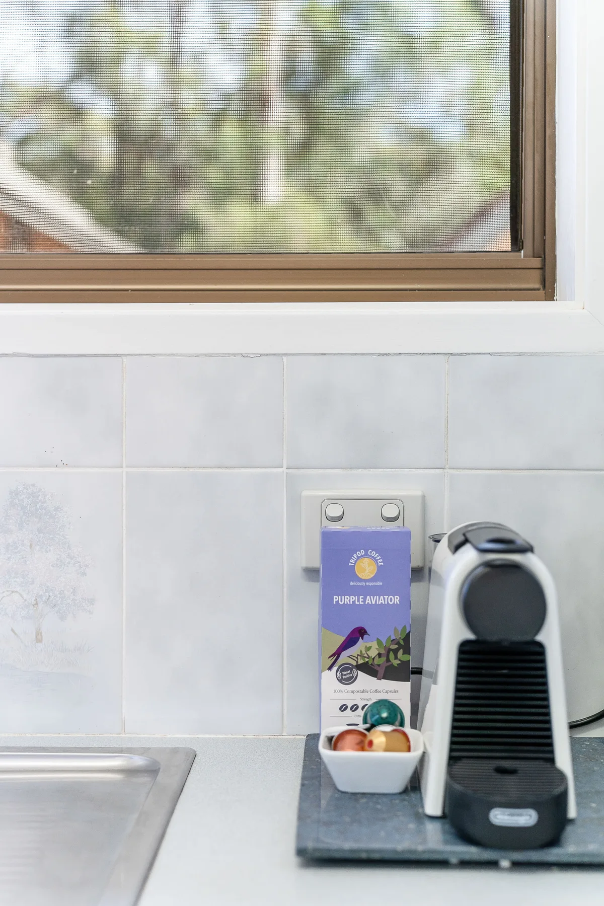 A kitchen counter with a coffee machine, fruit, and a window above.