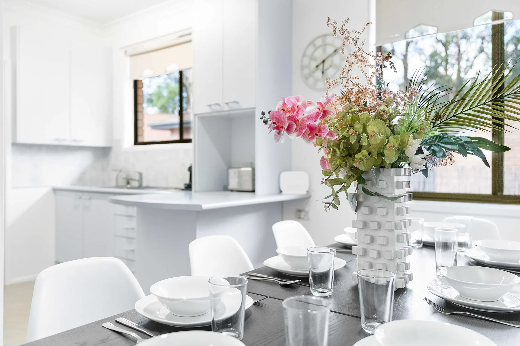 A bright dining area with table settings beside a white kitchen.