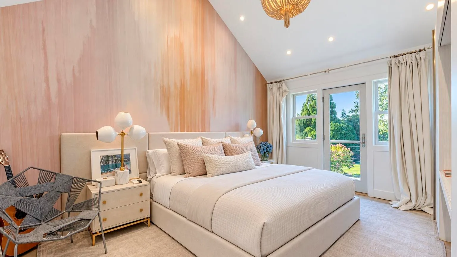 Un dormitorio con una cama bien tendida junto a ventanas altas y cortinas claras.