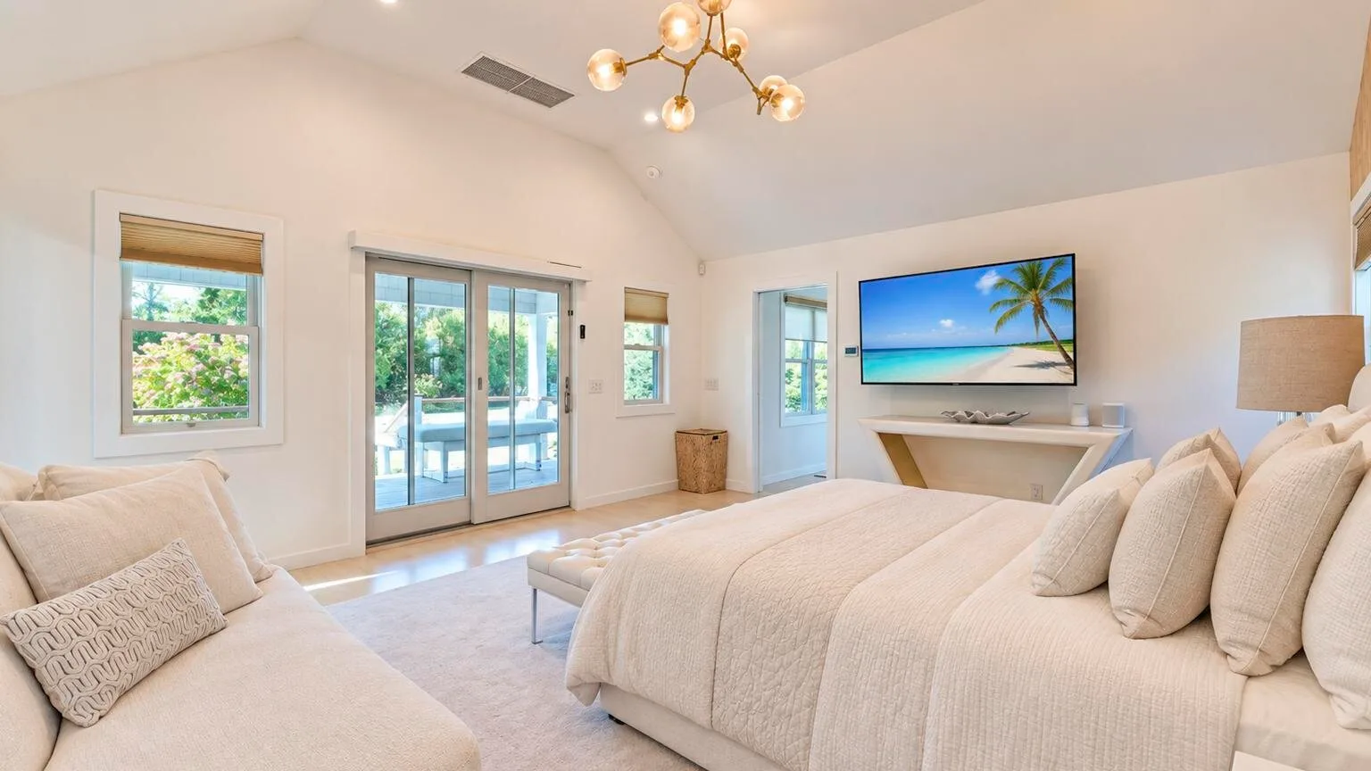 Un dormitorio luminoso con una cama grande, puertas de vidrio y un televisor en la pared.