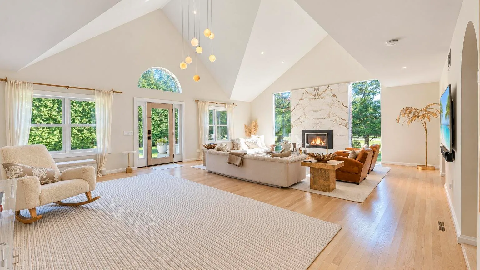 Una sala luminosa con techo alto, grandes ventanas y asientos alrededor de una chimenea.