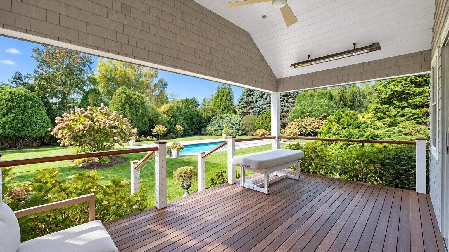 Una terraza cubierta da a un jardín paisajístico y una piscina.