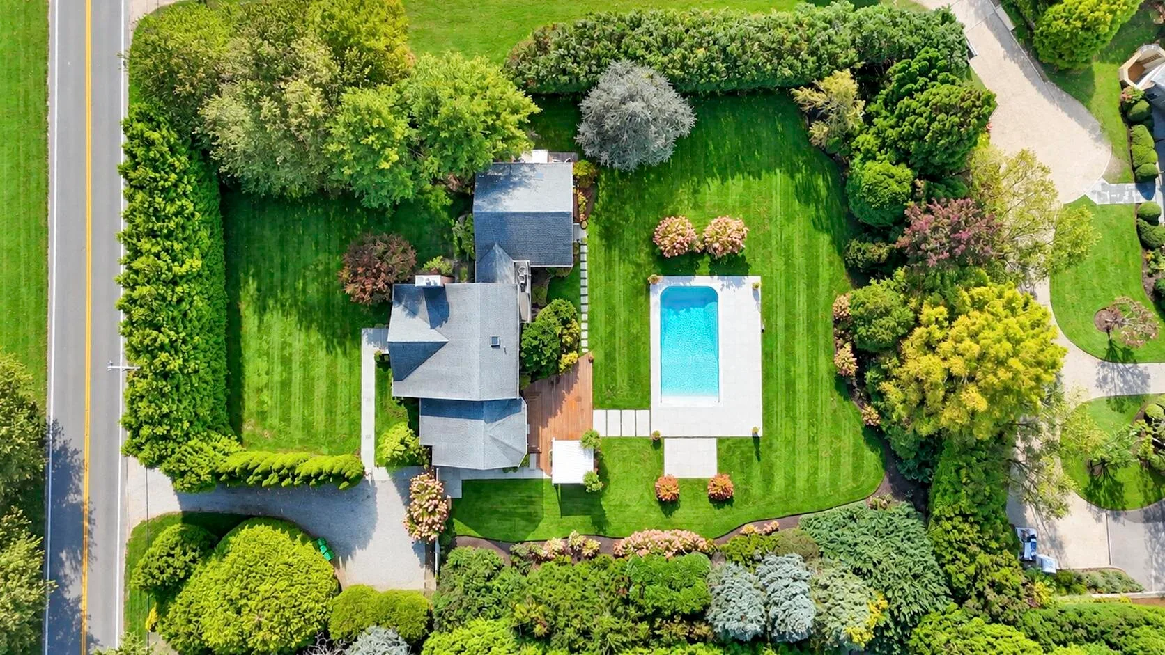 Vista aérea de una propiedad ajardinada con una casa, césped y piscina.