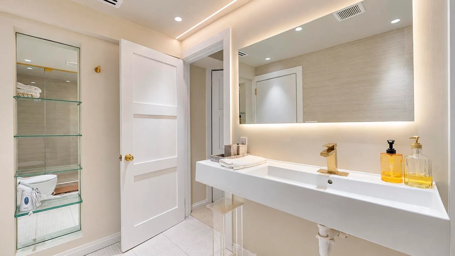 Un baño luminoso con un lavabo largo, espejo y estantes de vidrio.