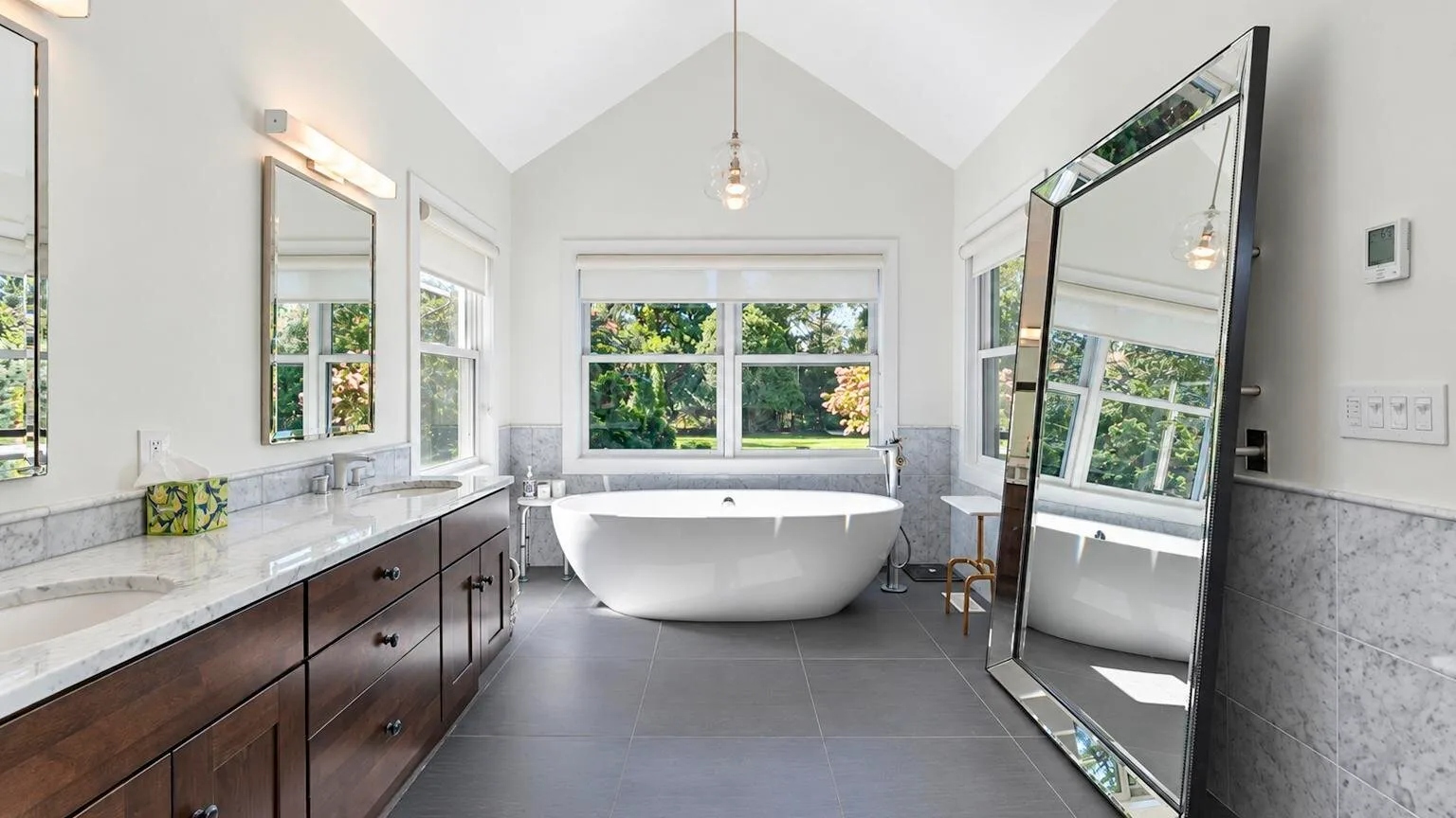 Un baño luminoso con bañera exenta, mueble de lavabo alargado y grandes ventanas.