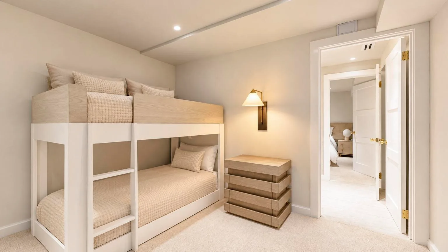 Un dormitorio luminoso con literas, una cómoda junto a la cama y una puerta abierta.