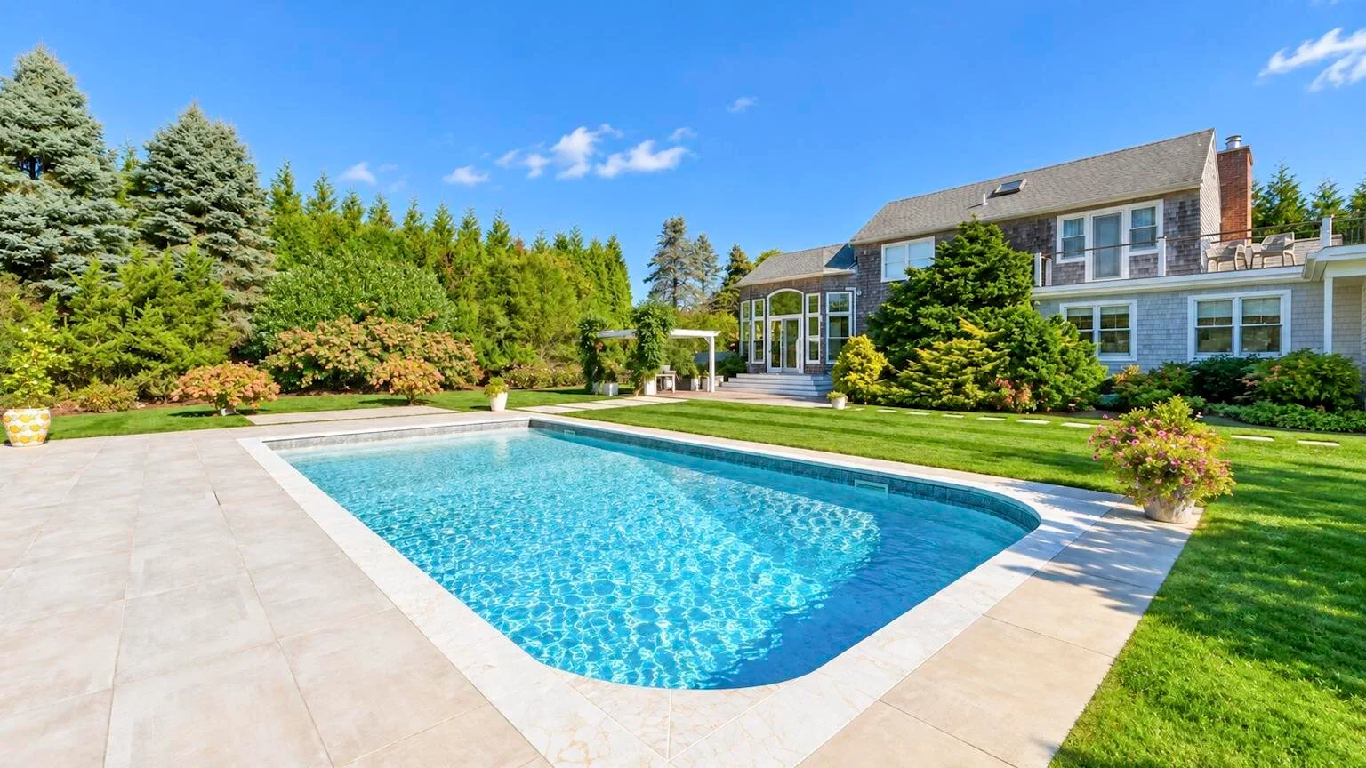 Una piscina está junto a una casa grande y un jardín cuidado.