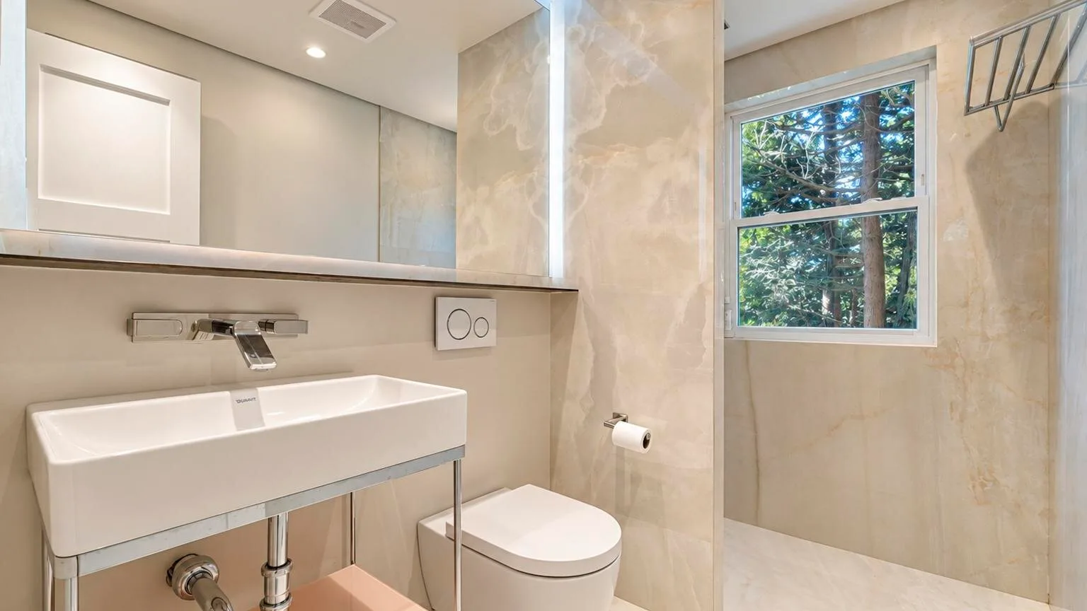 Un baño con lavabo montado en la pared, inodoro y ventana.