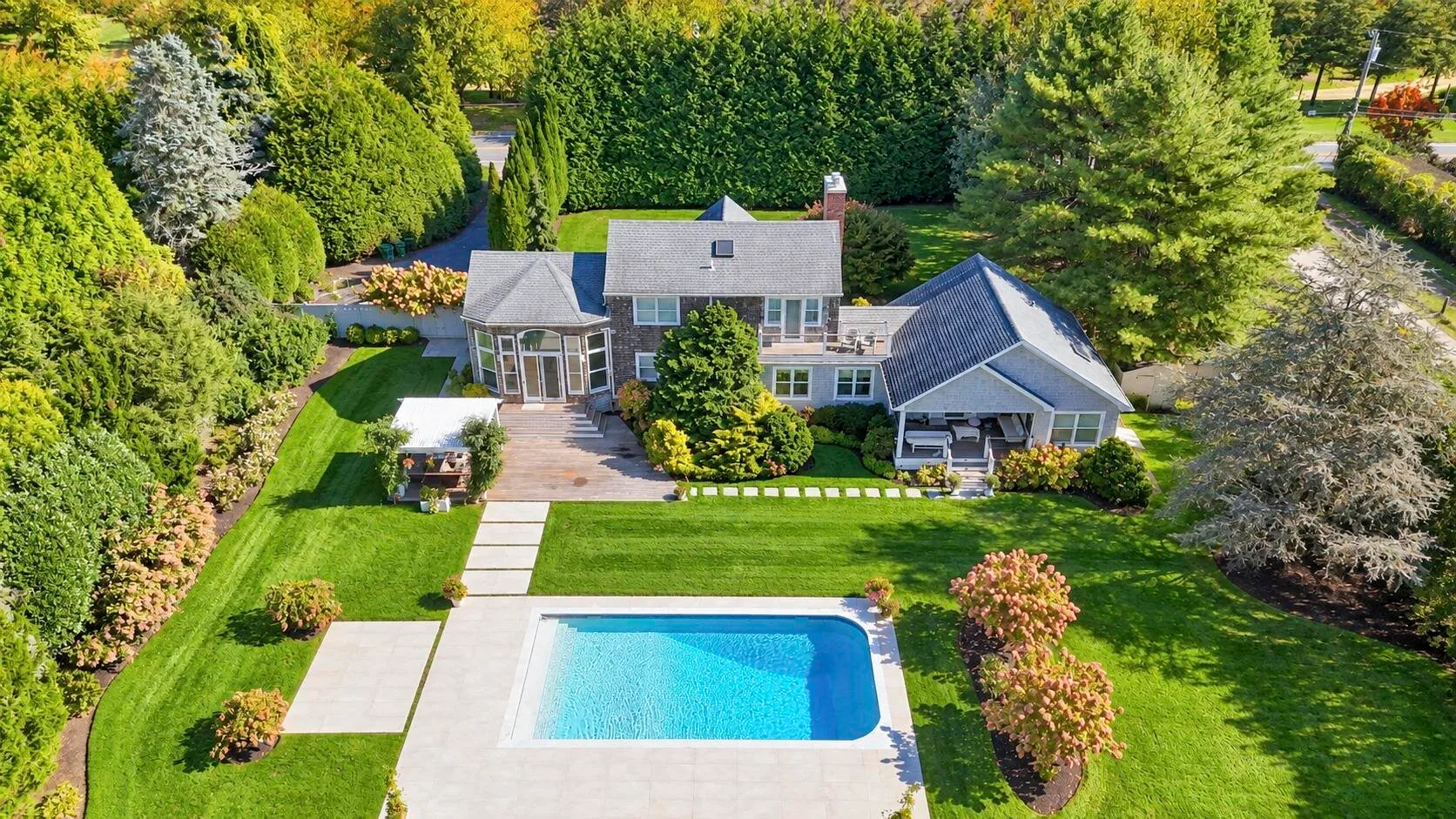 Vista aérea de una casa y una piscina rodeadas de césped y árboles.