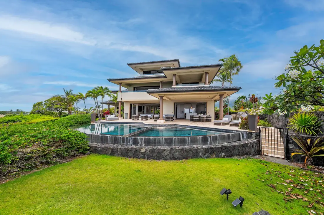 A modern house opens onto a curved swimming pool and a green lawn.