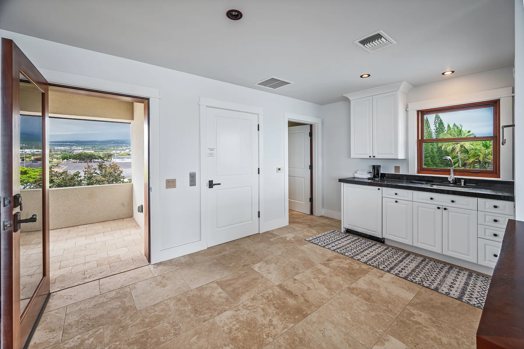 A bright kitchen opens onto a tiled balcony with a broad outdoor view.