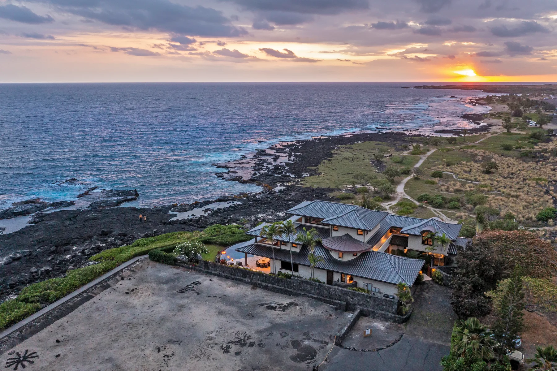 A coastal property sits beside rocky shorelines beneath a sunset sky.