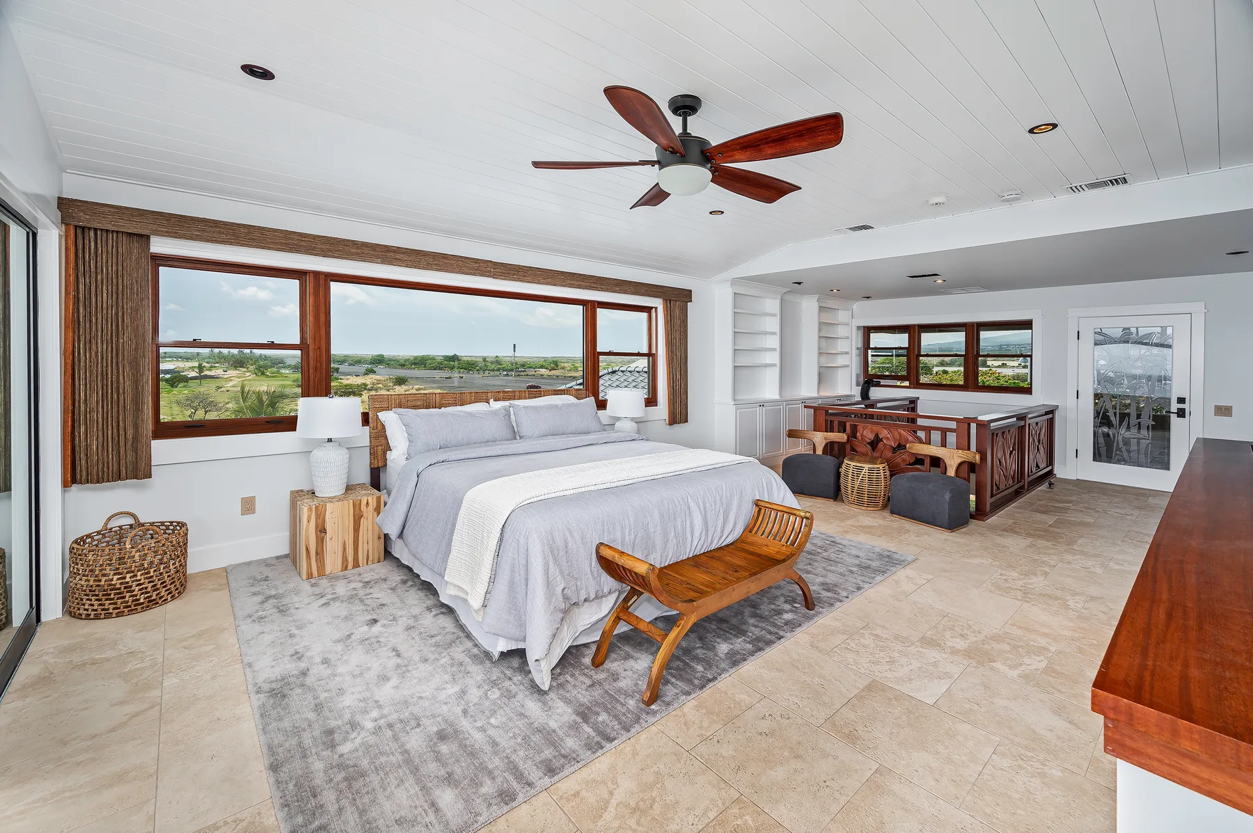 A bedroom with a large bed, wide windows, and a ceiling fan.