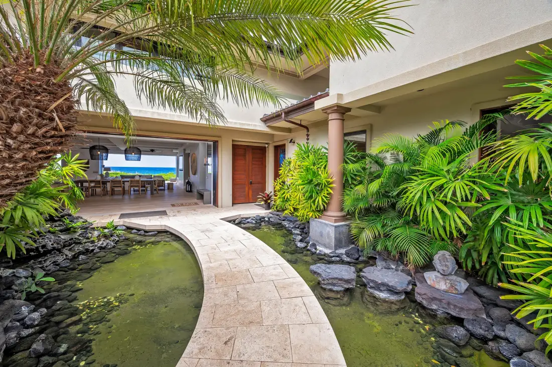 A tropical courtyard with a curved path beside a small pond and lush plants.