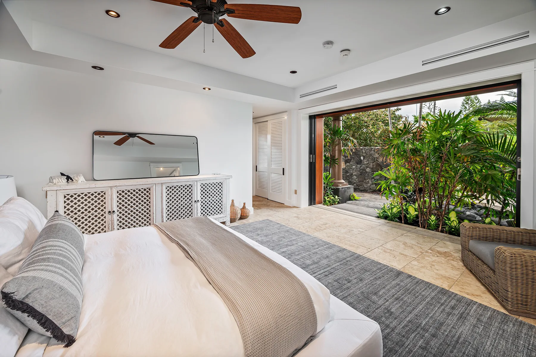 A bright bedroom opens onto a leafy patio through wide sliding glass doors.