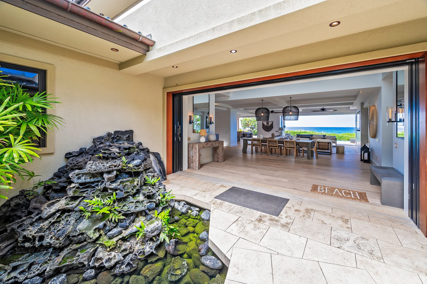 An open-air entry leads into a dining area beside a rocky water feature.