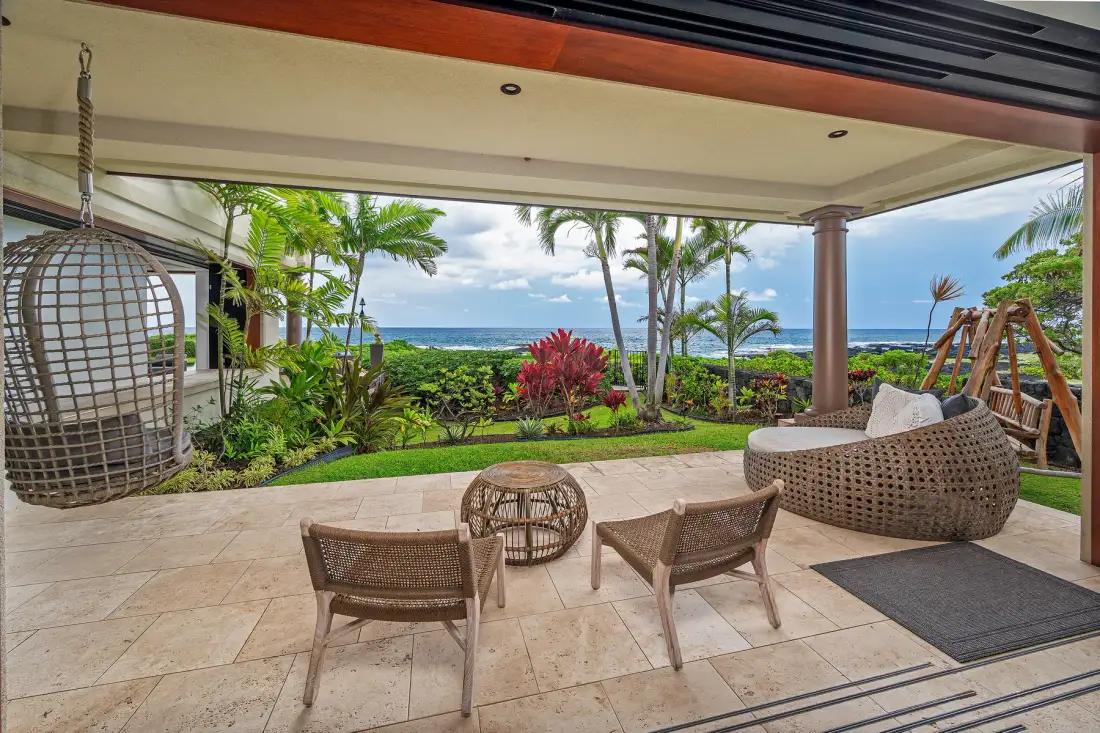 A covered patio opens onto a tropical garden, with outdoor seating and ocean views.