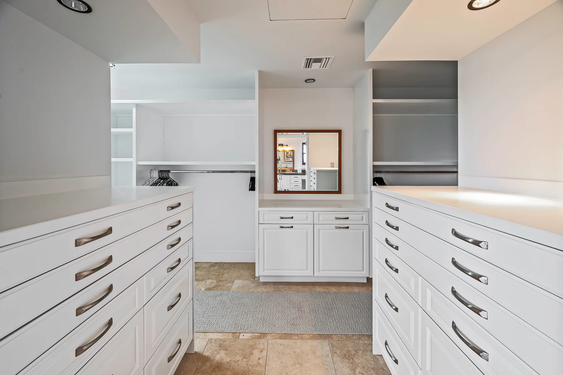 A bright walk-in closet with white drawers and a mirror above the central counter.