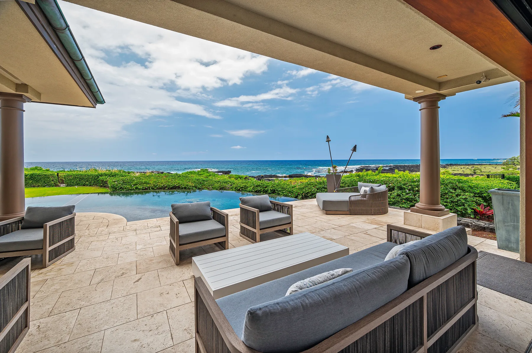 A covered outdoor patio with seating overlooks a pool and the ocean.