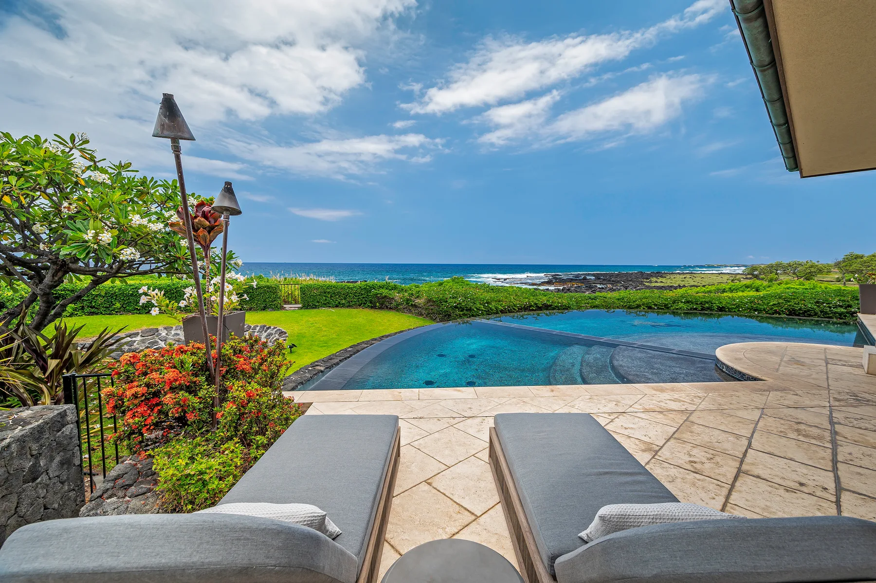 An outdoor pool overlooks the ocean, with lounge seating on a paved patio.