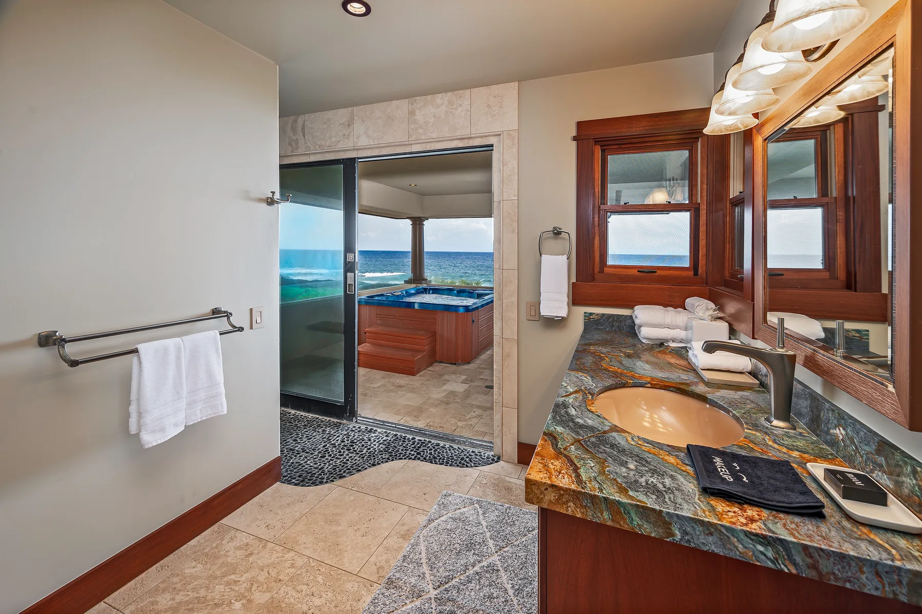 A bathroom with a stone countertop and a bathtub beside large windows overlooking the water.