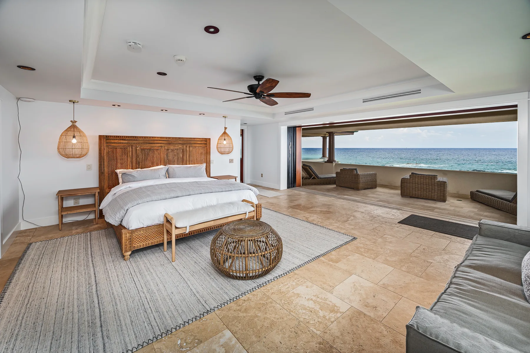 A bedroom with a woven bed frame, rug, and a wide ocean view.