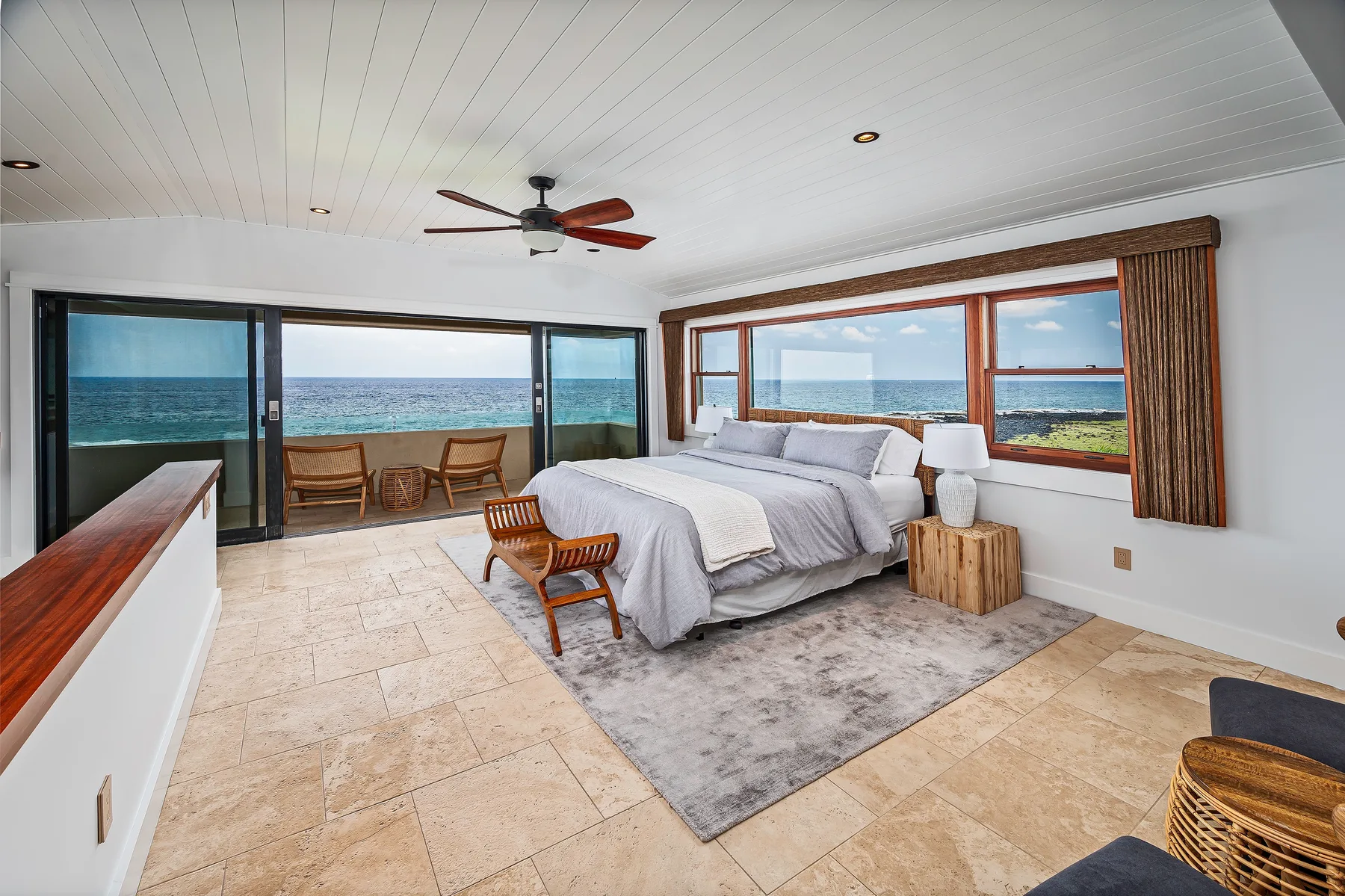 A bedroom with a bed beside large windows overlooking the ocean.