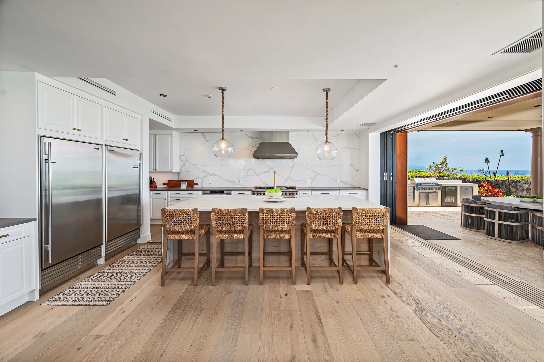 A bright kitchen with a long island and seating opens onto an outdoor terrace.