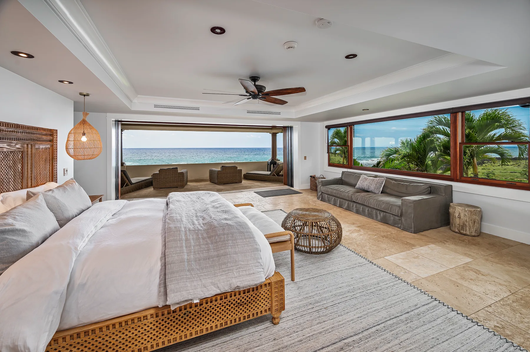 A bright bedroom opens onto a living area with large windows overlooking the ocean.