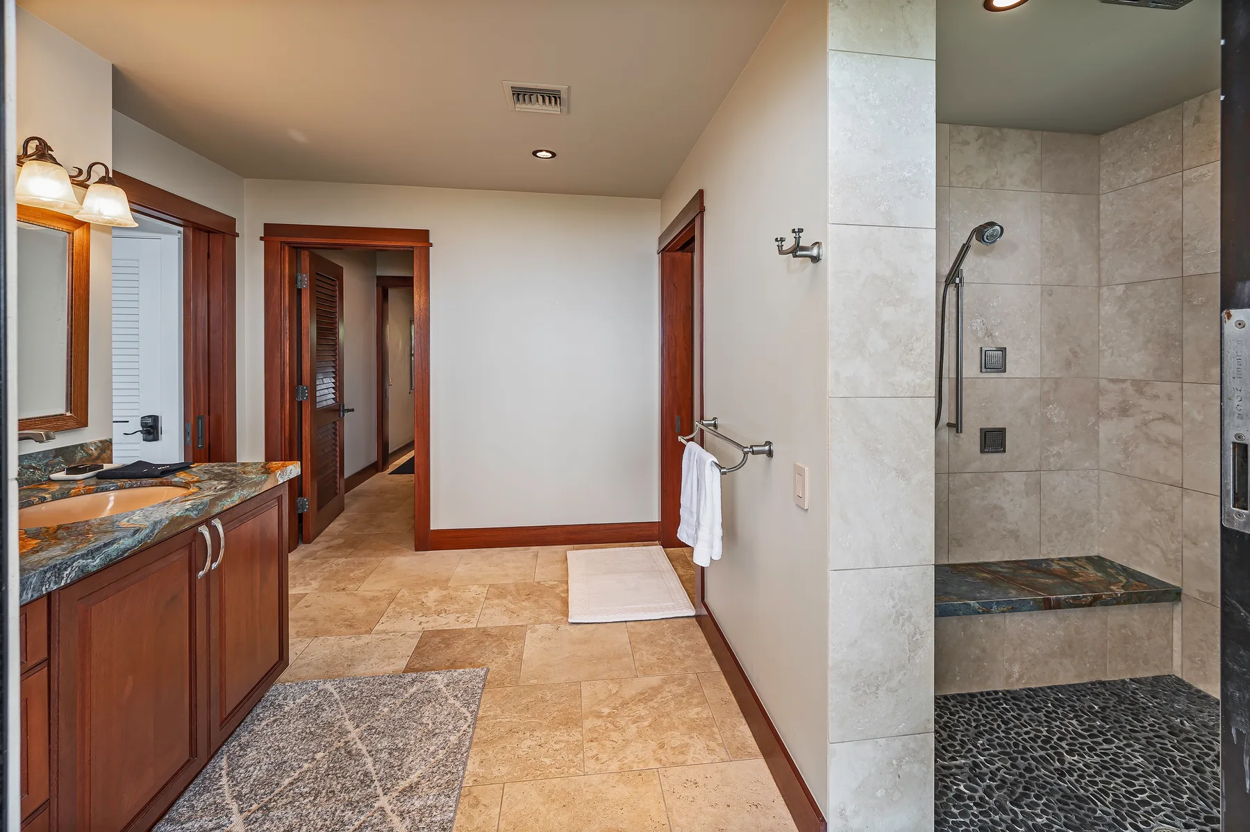 A bathroom with a vanity, tiled floor, and open shower area.