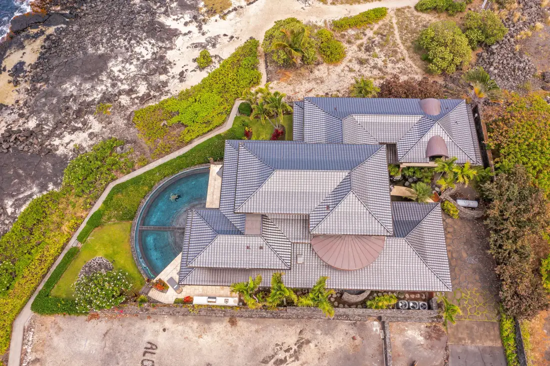 An aerial view of a large house with a curved swimming pool and surrounding greenery.