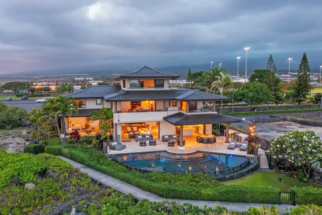 A modern house overlooks a curved swimming pool and landscaped grounds.