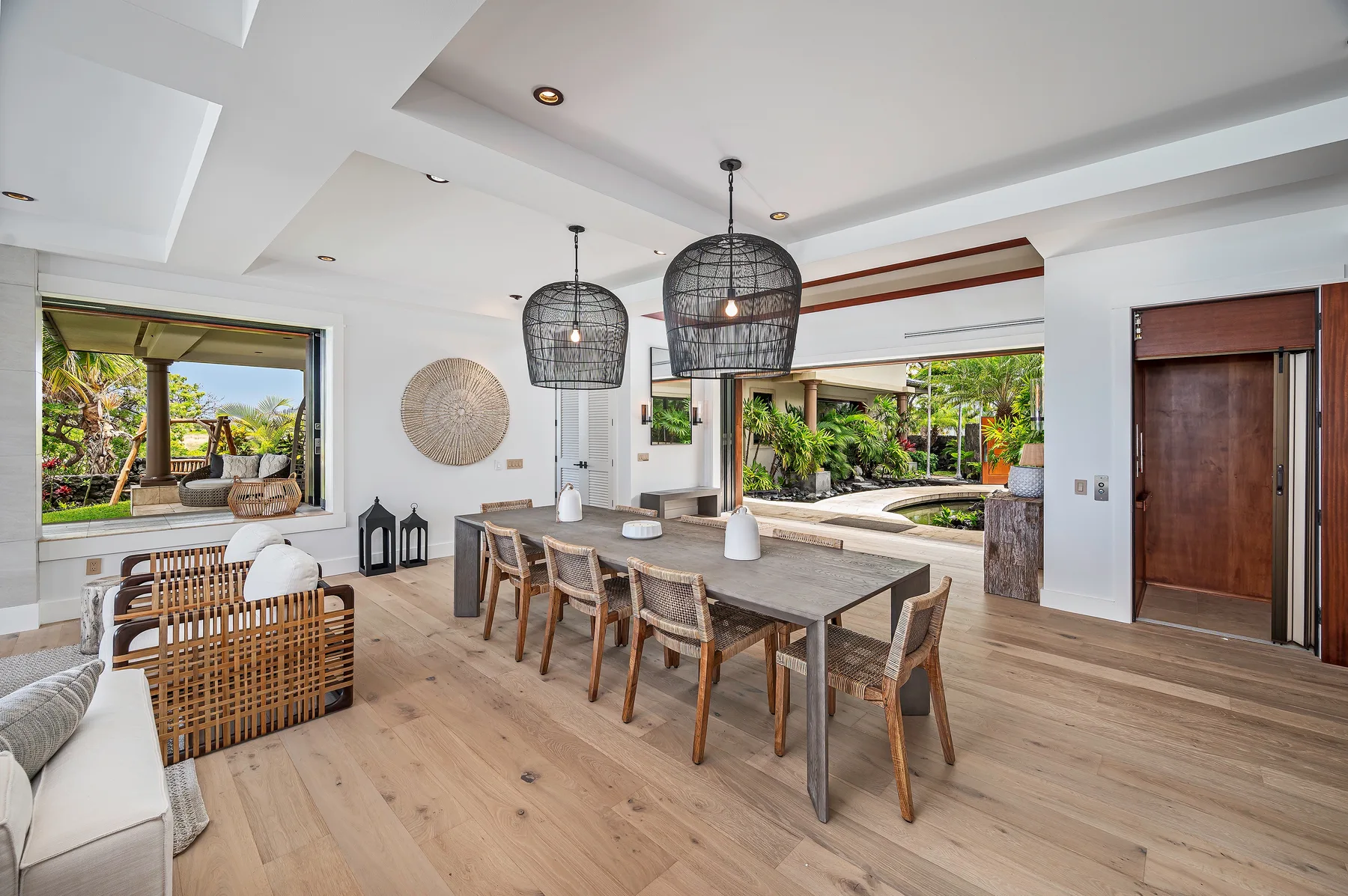 A dining area with a long table and pendant lights, opening onto a garden.