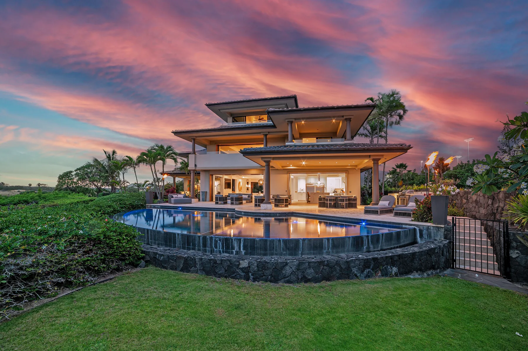 A modern house opens onto a curved swimming pool beneath a colorful evening sky.