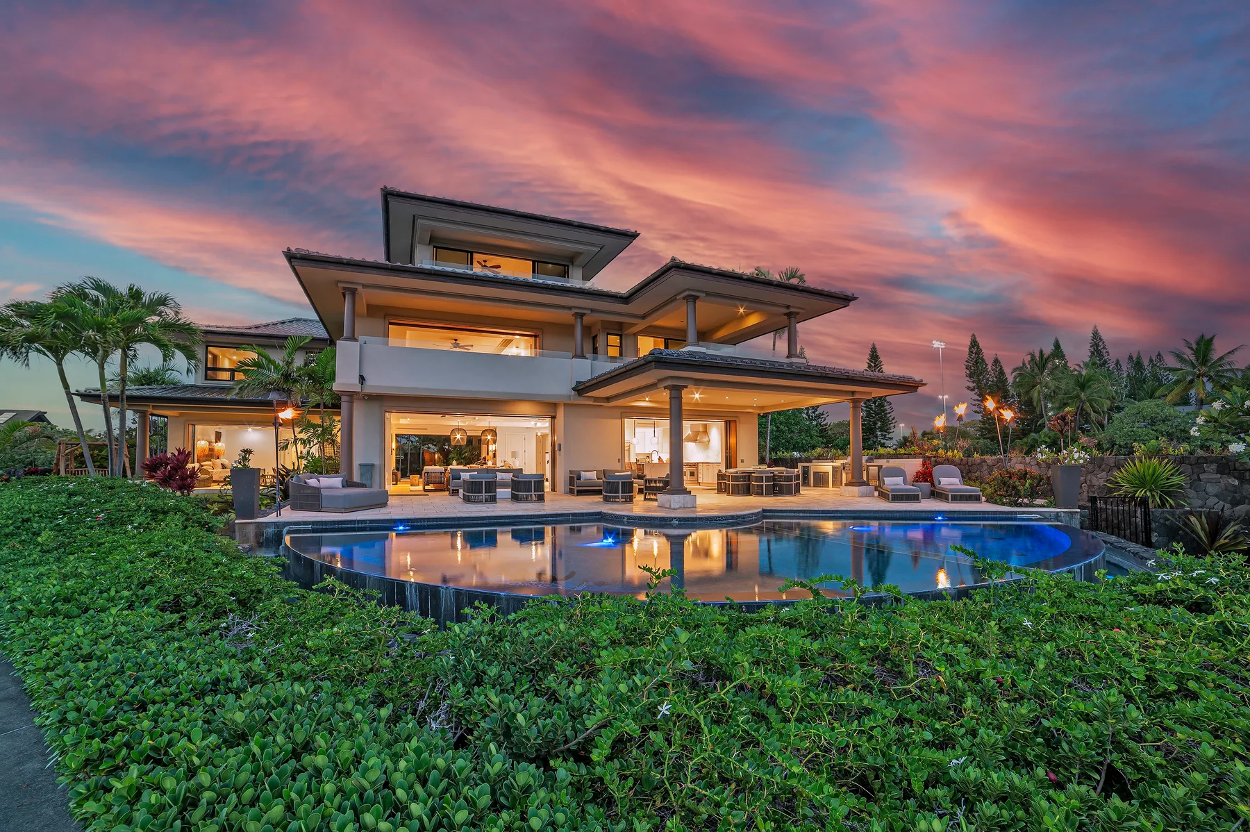 A modern house with a swimming pool sits amid lush greenery at sunset.