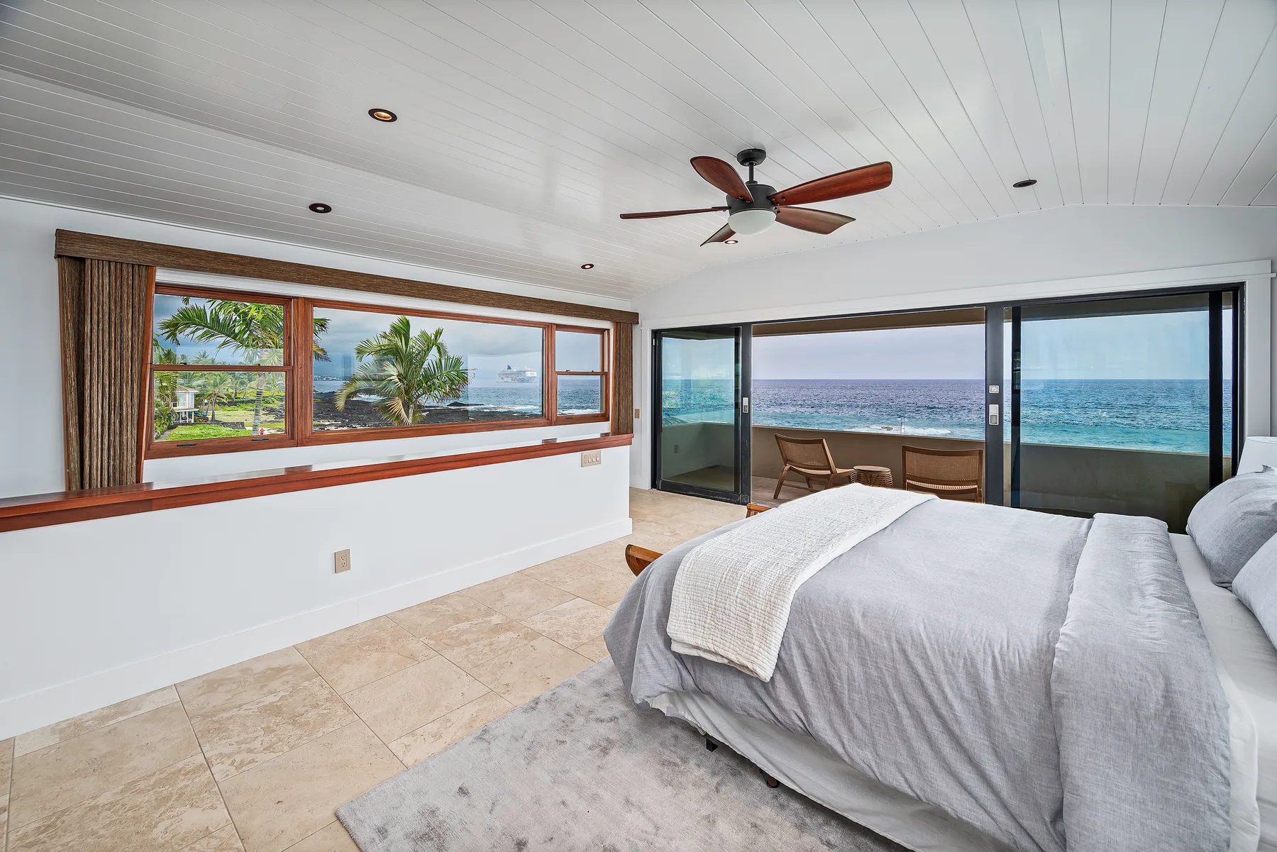 A bedroom with a bed beside large windows overlooking the ocean.