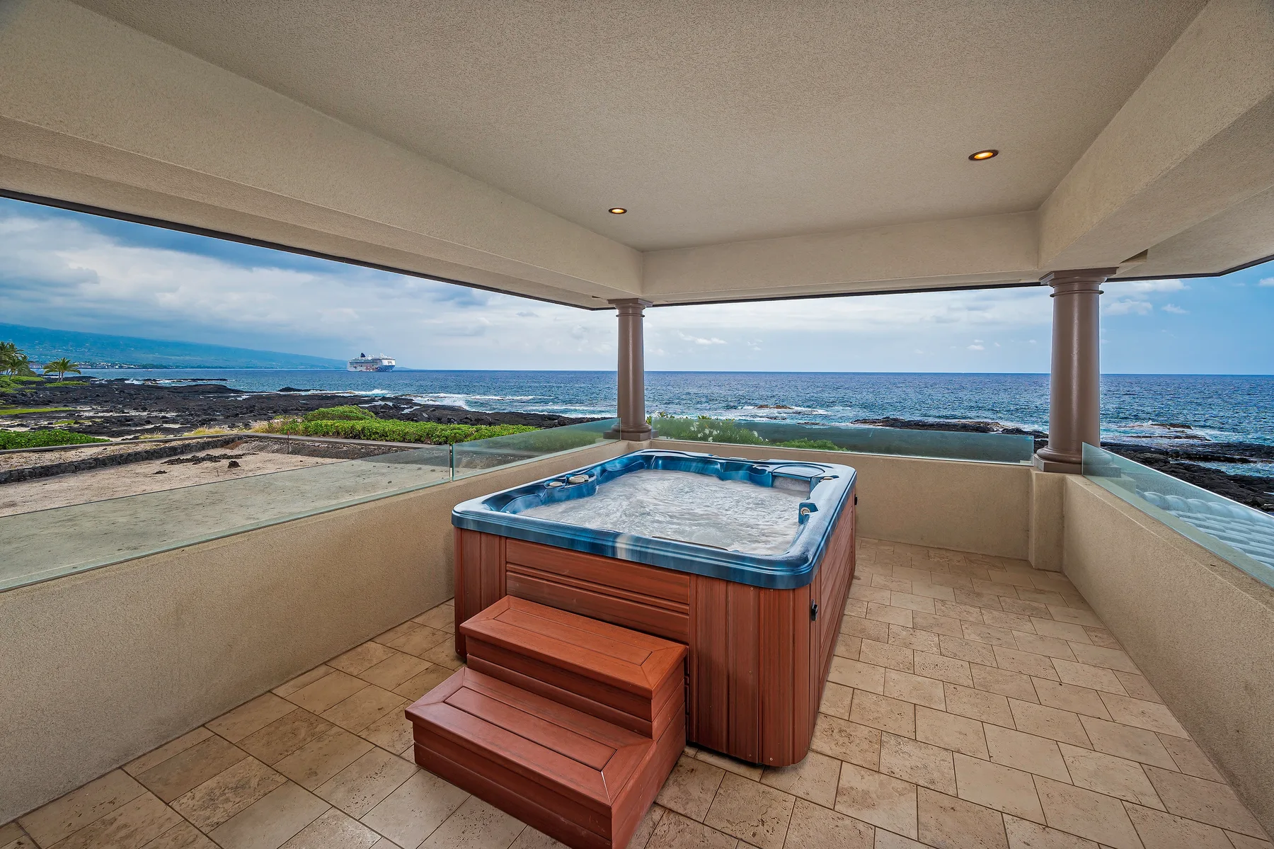 A covered outdoor patio with a hot tub overlooking the ocean.