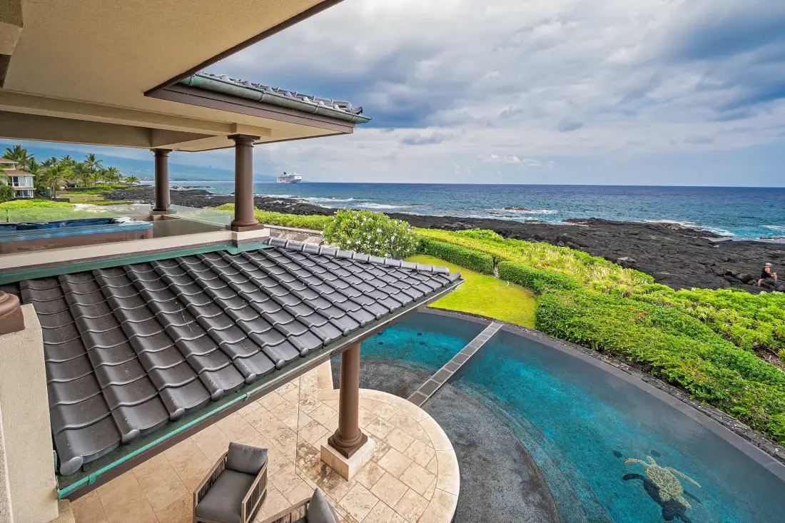 A seaside patio overlooks a swimming pool and the ocean.