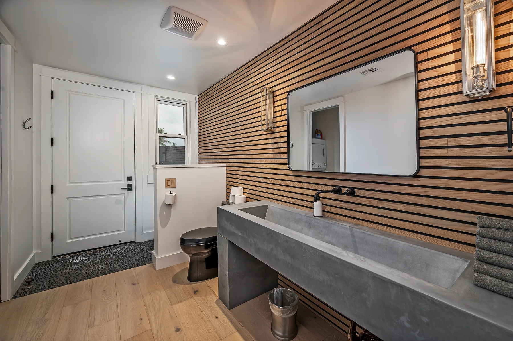 A modern bathroom with a long vanity, wall mirror, and wood slat accents.