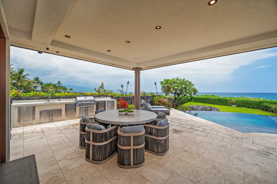 A covered outdoor dining area overlooks a pool and the ocean.