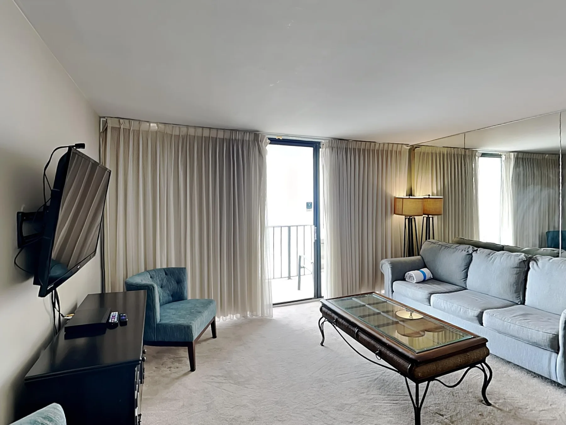 A living room with seating, a coffee table, and curtains beside a glass door.