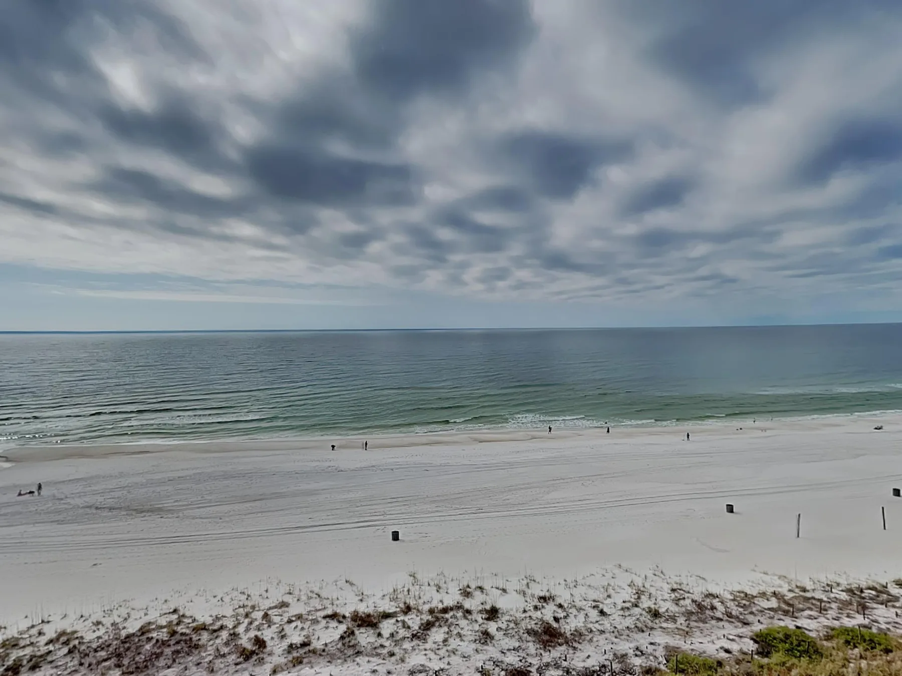 A broad sandy beach meets calm water beneath a cloudy sky.