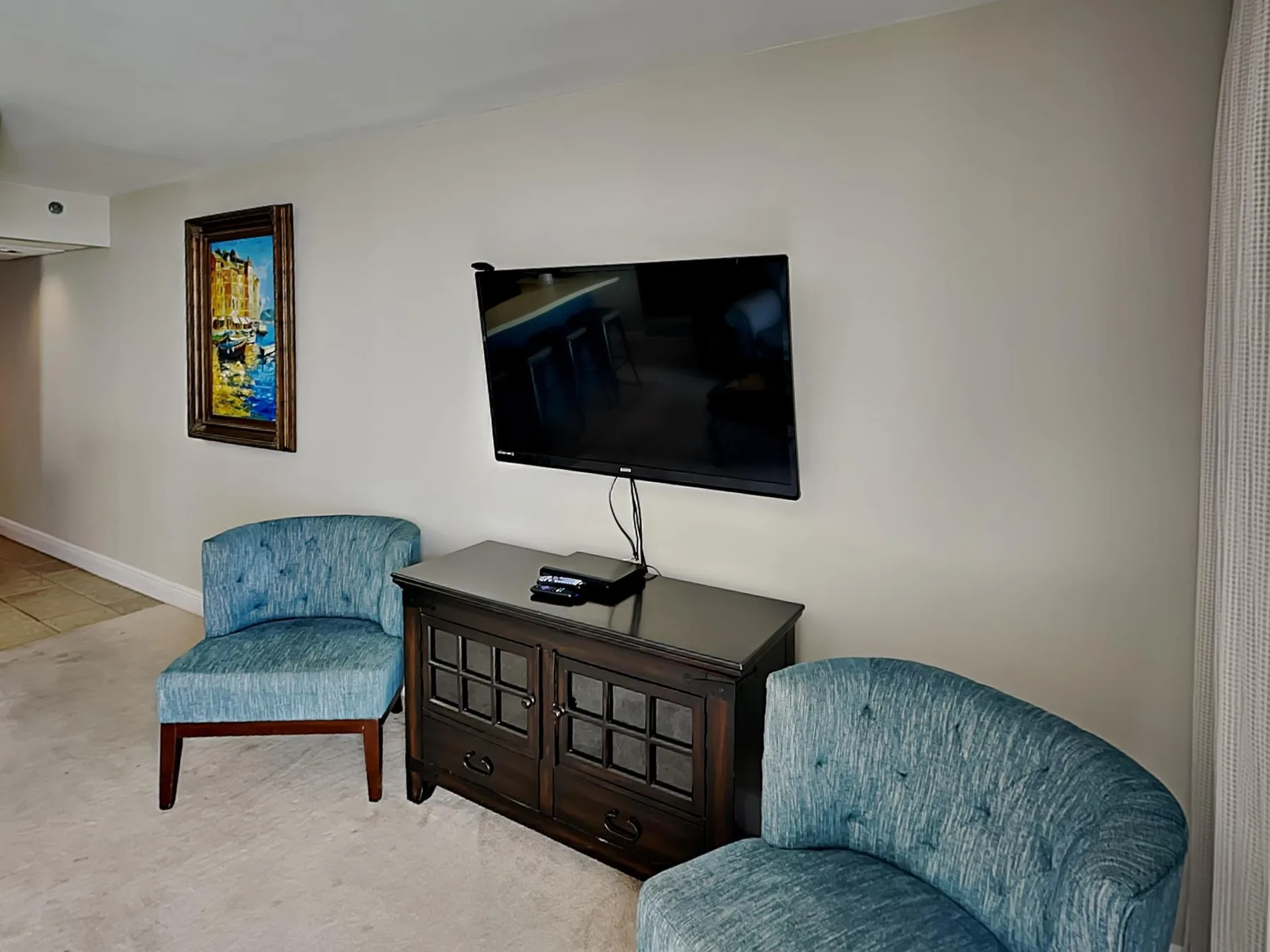 Una zona de estar con un televisor sobre una consola de madera y dos asientos tapizados.