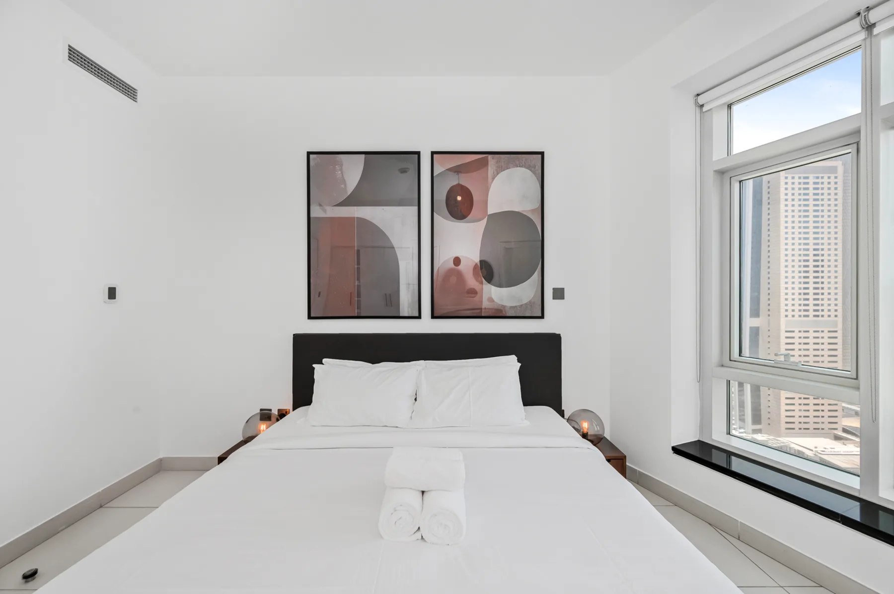 Un dormitorio luminoso con una cama tendida y arte abstracto sobre el cabecero.