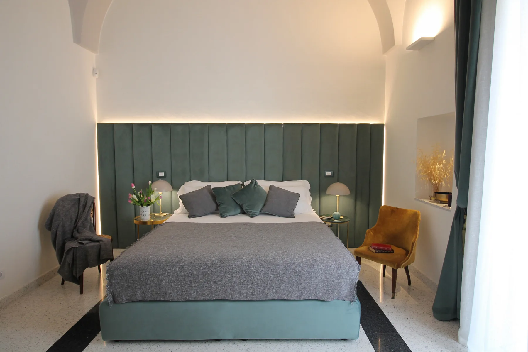 A bedroom with a large bed, dark upholstered headboard, and matching bedside tables.