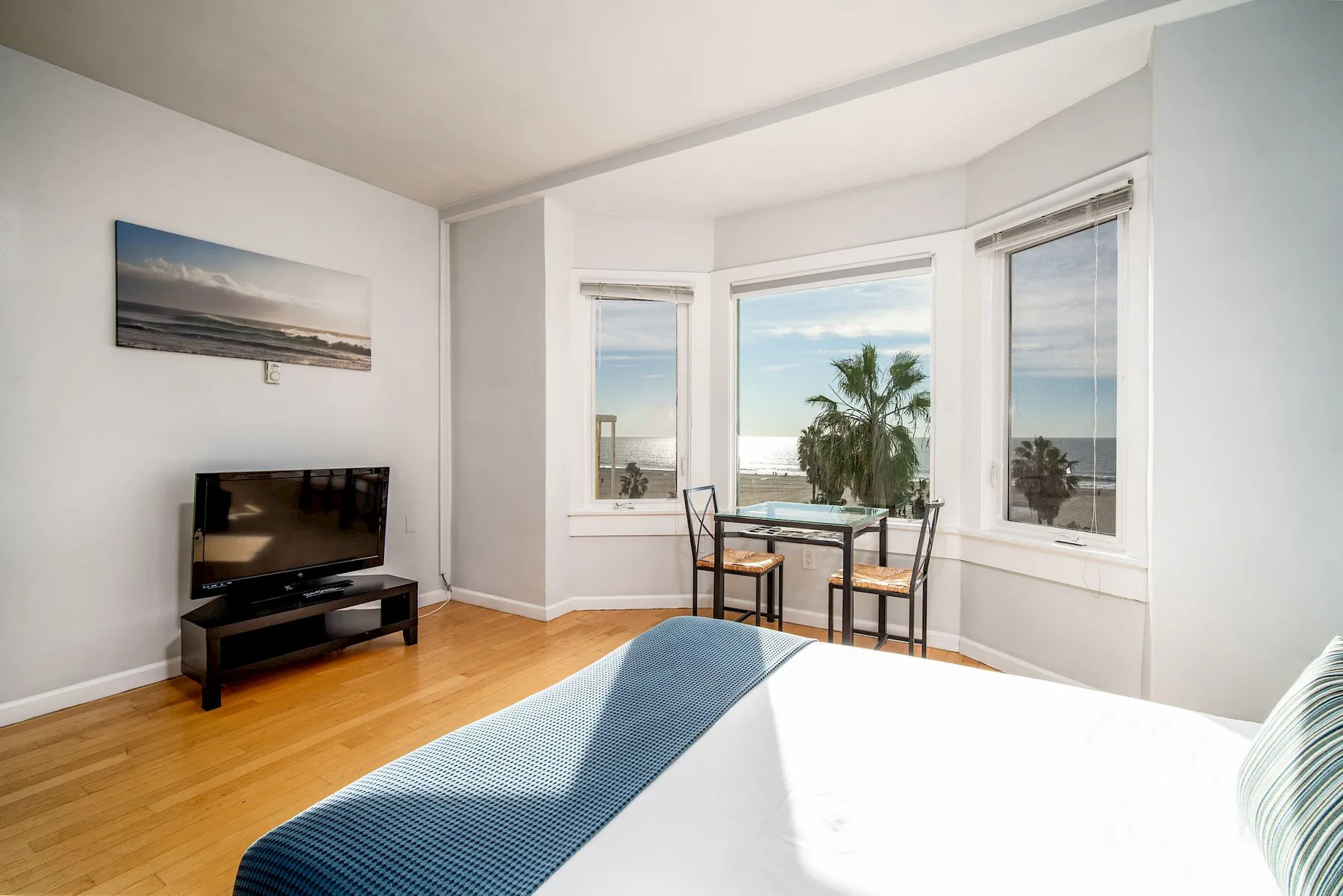 Dormitorio con cama, televisor, mesa de comedor y ventanas con vistas al mar.