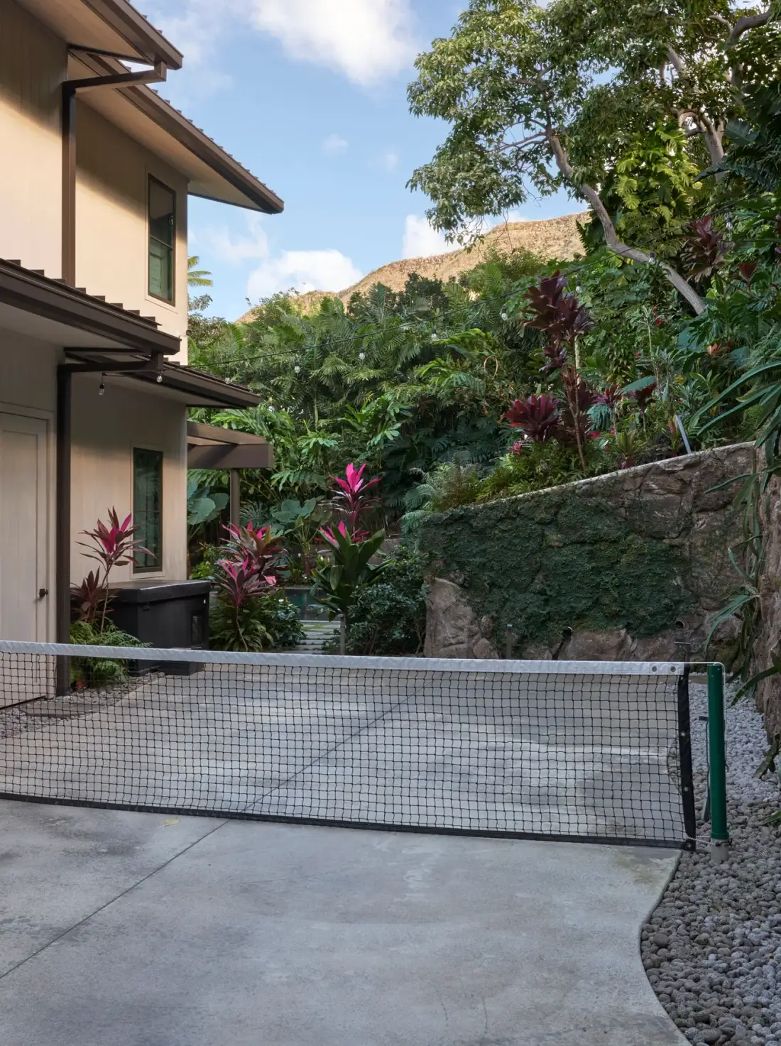 An outdoor court with a net, surrounded by lush tropical plants.
