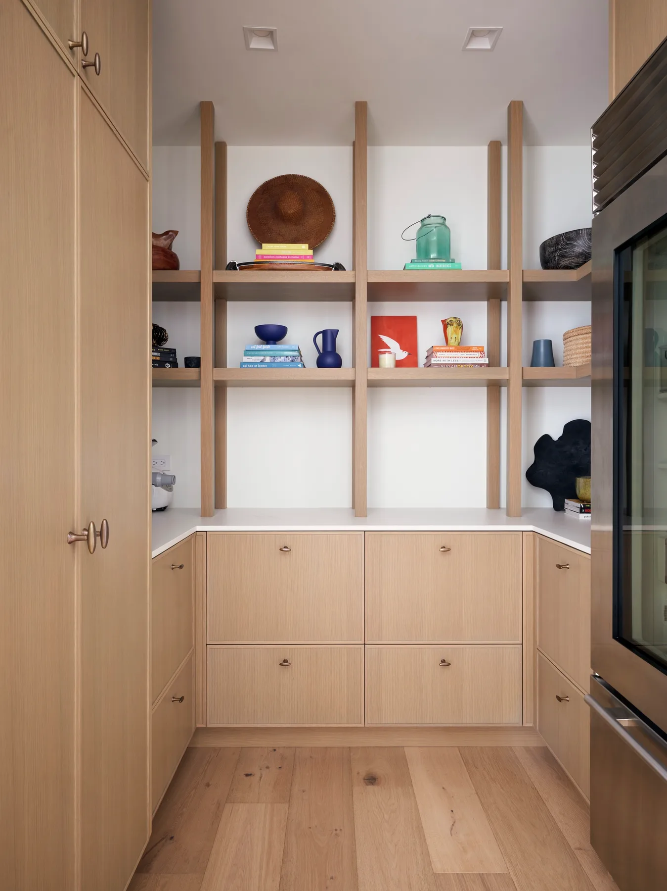 A built-in storage area with open shelves above light wood cabinets.